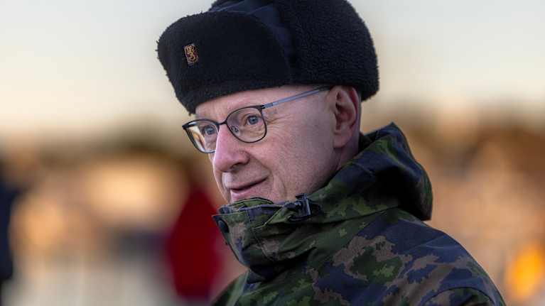 Silmälasipäinen mies pukeutuneena Puolustusvoimien M05-kuvioiseen takkiin ja mustaan Puolustusvoimien karvalakkiin ulkoilmassa.