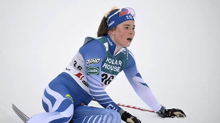 Krista Pärmäkoski maalissa istumassa sukset jalassaan ja sauvat kädessä.