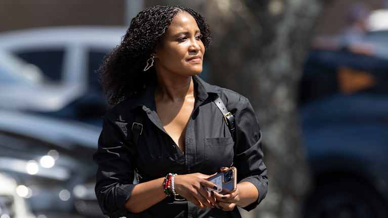 Mustiin pukeutunut tummaihoinen nainen kadulla, pitää käsissään kännykkää.