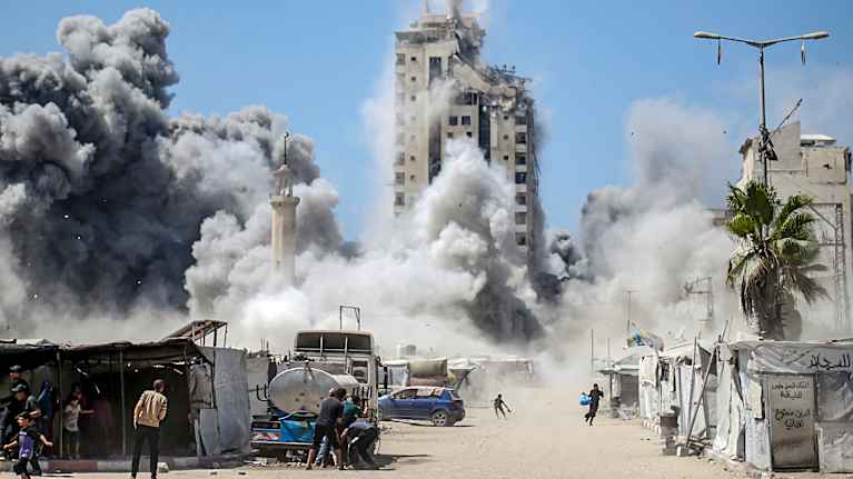 Savupatsas kohoaa ilmaan rakennusten ja raunioiden keskeltä.