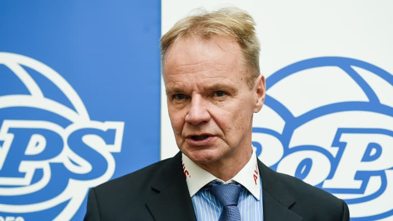 Mies seisoo ROPS mainosseinän edessä ja vastaa kysymyksiin.