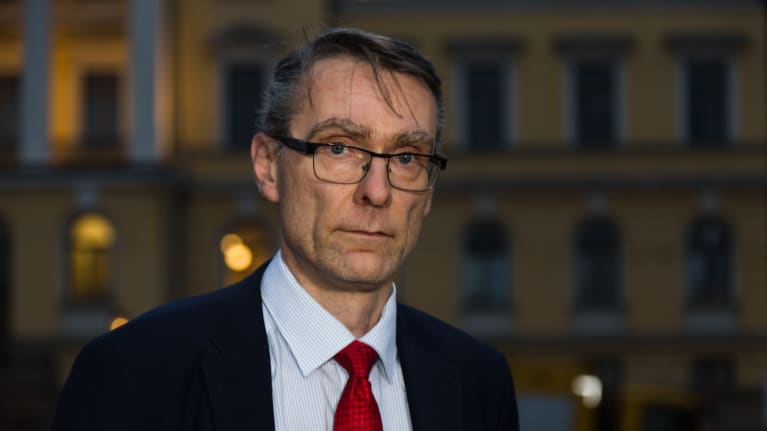 Tuomas Pöysti pimenevässä illassa Senaatintorilla. Tuomas on pukeutunut tummansiniseen pukuun. Vaaleansinisen kauluspaudan parina on punainanen kravatti ja rintataskusta pilkistää punaisilla ympyröillä koristeltu valkonen liina.