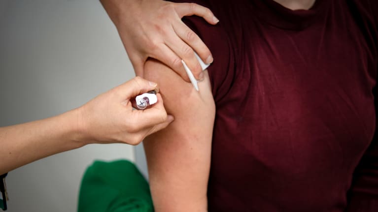 Hoitaja pistää rokotusta olkavarteen.