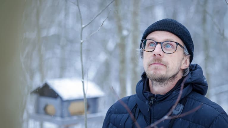 Heikki Helle katsoo taivaalle talvisessa maisemassa. Taustalla lintulauta.