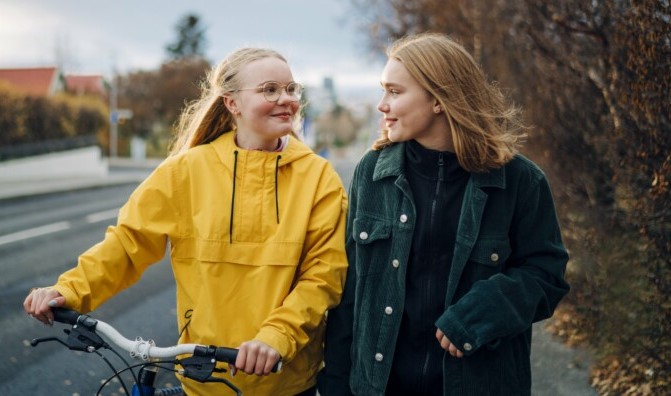 Kaksi nuorta kävelee vierekkäin kadulla. Toinen taluttaa polkupyörää.