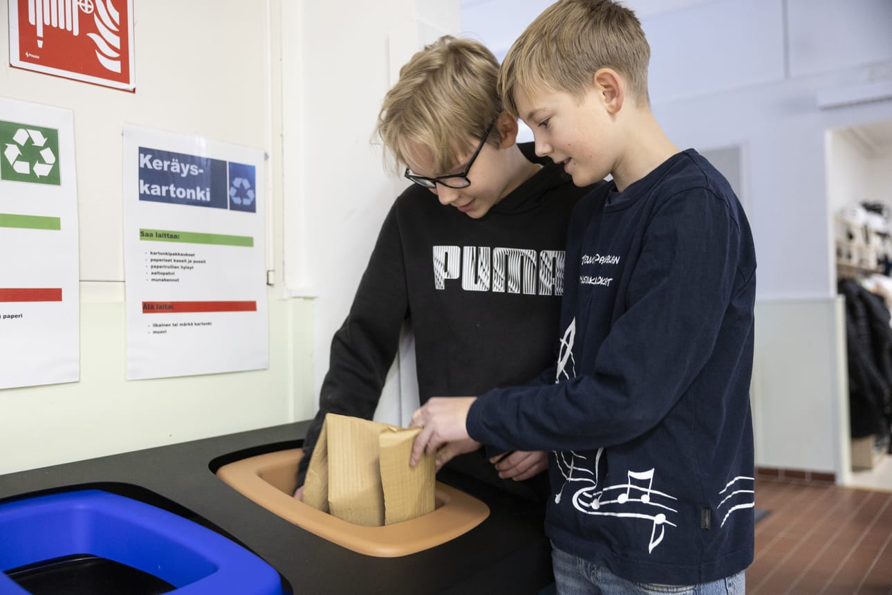Lukas Urpelainen (vas.) ja Joan Närhi täyttävät keräyskartonkiastiaa. Lajittelu on tuttua jo kotoa.