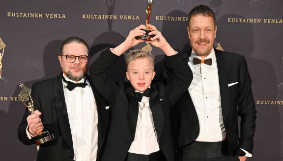 Juha Korhonen sekä Osmo ja Mikko Peltola poseeraavat Venla-gaalan punaisella matolla. Kaikki ovat pukeutuneet mustiin smokkeihin. Juha Korhonen ja Osmo Peltola pitelevät käsissään Venla-palkintoja, Osmo päänsä yläpuolella.