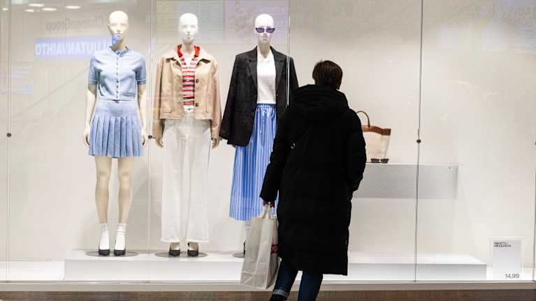 Henkilö katselee vaateketjun näyteikkunan asusteita.