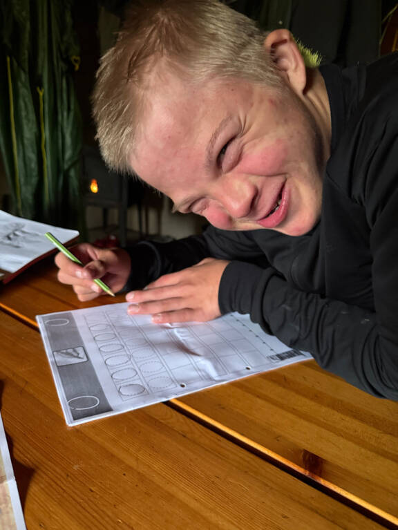 Hymyilevä Osmo Peltola tekee paperilla olevaa tehtävää.