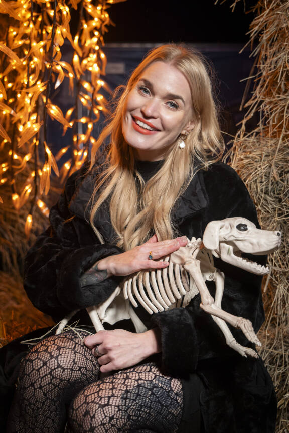 Iida Ketola poseeraa halloween-teemaisessa kuvassa mustassa asussa istuen. Sylissään hän pitää koiran luurangolta näyttävää lelua.