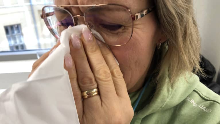 Nainen niistää nenäänsä tuskaisen näköisenä.