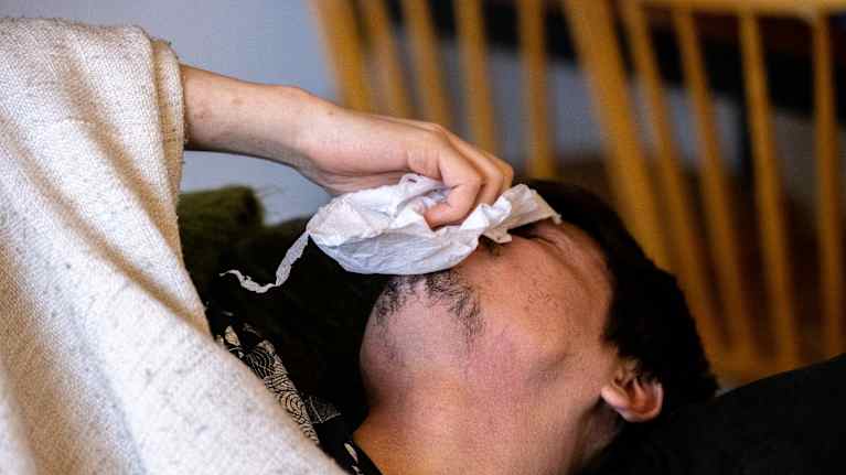 Mies makaa sohvalla viltin alla ja niistää nenäänsä.