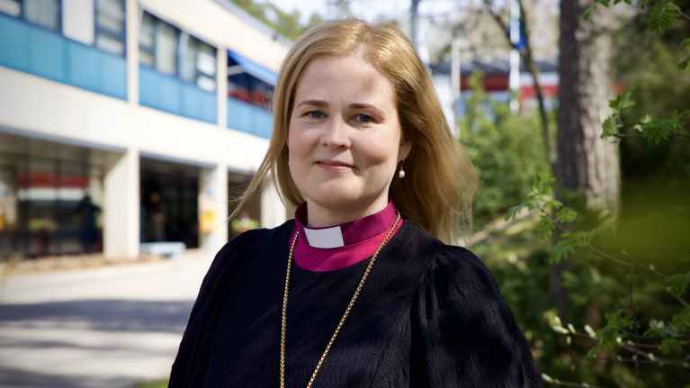 Piispa Mari Leppänen seisoo rakennuksen edessä ja katsoo kohti kameraa.