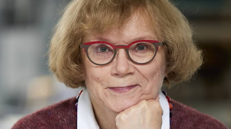 Marja Jylhä nojaa kämmeneensä ja katsoo suoraan kameraan.