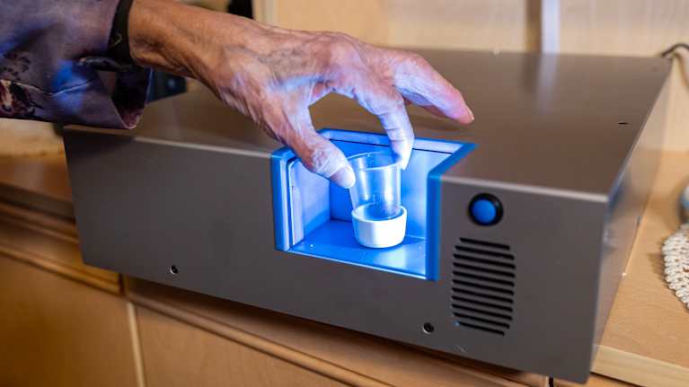 Vanhuksen käsi ottaa pienen lääkekupin lääkeautomaatista.