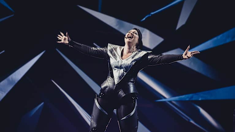 Neea River laulamassa UMK-lavalla suurella tunteella. Riverin yllä on musta esiintymiasu ja lavan valot ovat siniset.