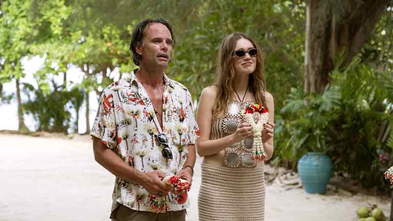 Mies ja nainen trooppisessa ympäristössä, molemmat pitävät käsissään koristeellisia kukka-asetelmia.