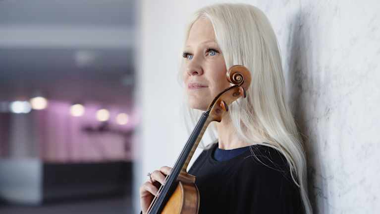 Linda puolikuvassa sivuittain kameraan. Hän pitelee viulua vasten vartaloa ja katsoo levollisesti kohti kaukaisuutta.