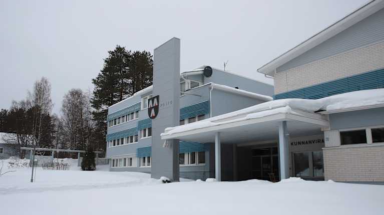 Vaaleasta tiilestä rakennettu virastotalo jonka seinässä Posion kunnan vaakuna.