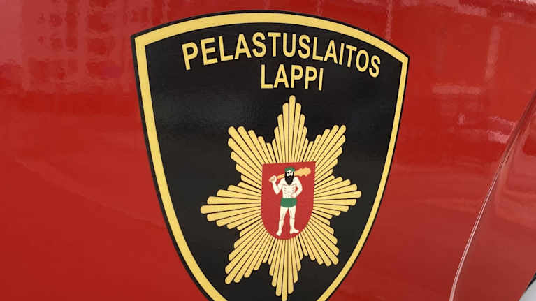 Lapin pelastuslaitoksen vaakuna punaisen hälytysajoneuvon ovessa.