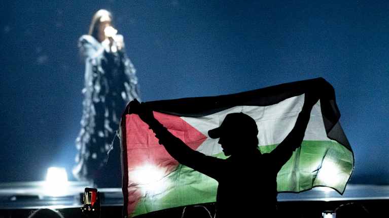 Henkilö pitelee yleisössä Palestiinan lippua laulajan esiintyessä lavalla.