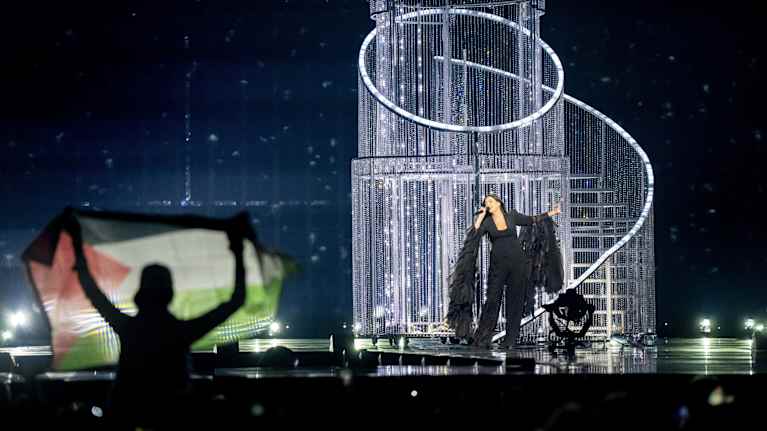 Israelin Yuval Raphael Euroviisulalla. Henkilö näyttää etualalla Palestiinan lippua. 