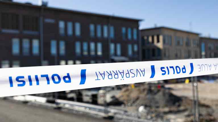 Vähäjärven valkotiilinen koulurakennus suorakaiteisine ikkunoineen aurinkoisena kesäpäivänä. Etualalla poliisin asettama valkosininen nauha.