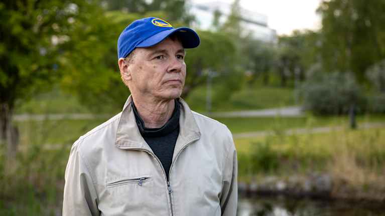 Juristi Olli Rauste puolilähikuvassa . Taustalla näkyy vihreää kasvillisuutta. Päässä hänellä on sininen lippalakki.