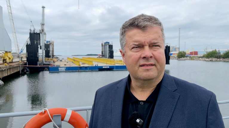 RMC toimitusjohtaja Mika Nieminen lähikuvassa, taustalla telakkanostureita.