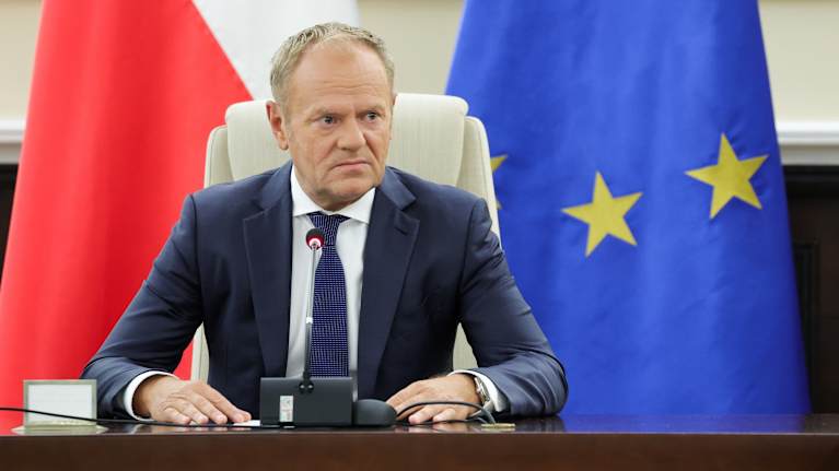Pulan pääministeri Donald Tusk Puolan ja EU:n lippujen edessä.
