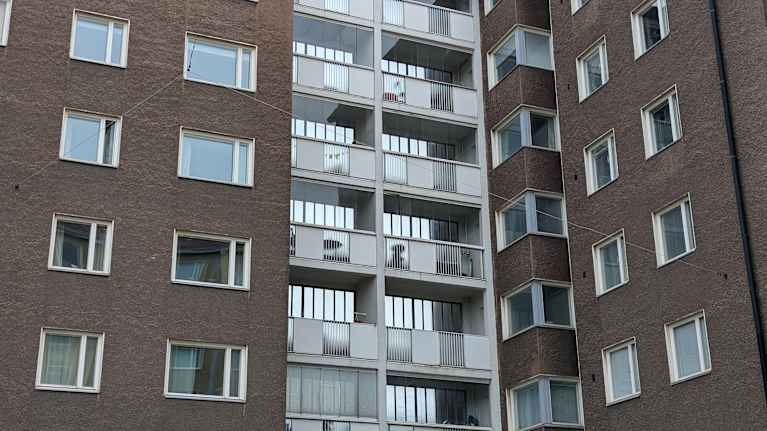 Vanha monikerroksinen kerrostalo, jonka yhdeltä parvekkeelta puuttuu vaalea levy.