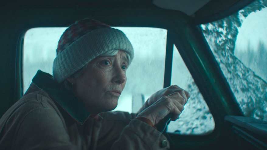 Vaaleasävyinen kuva, jossa vanha nainen ajaa pipo päässään autolla talvisissa olosuhteissa. Kuva auton sisältä.