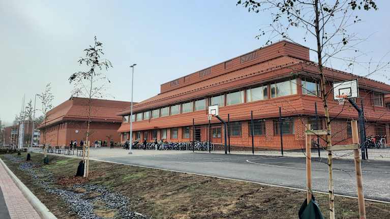 Punertava kaksikerroksinen koulurakennus. Polkupyöriä pihalla. 