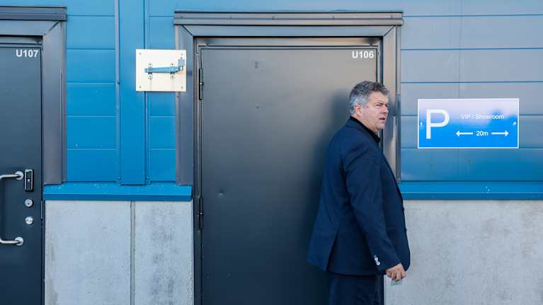 Siniseen pukuun pukeutunut mies avaamassa sininseinäisen rakennuksen ovea.