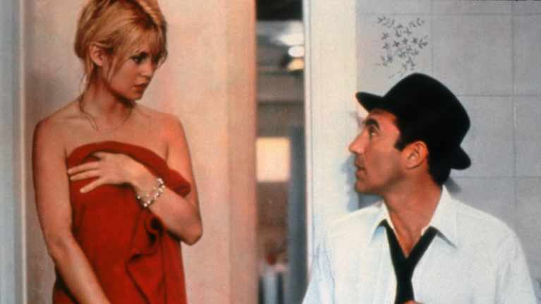 Punaiseen pyyhkeeseen kietoutunut Brigitte Bardot puhuu Michel Piccolille, jolla on valkoinen kauluspaita, musta kravatti ja musta huopahattu.