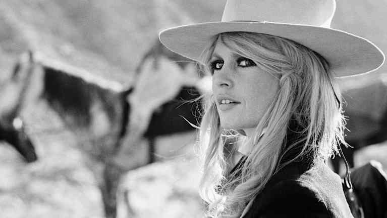 Brigitte Bardotilla cowboyhattu päässään ja taustalla on hevosia.