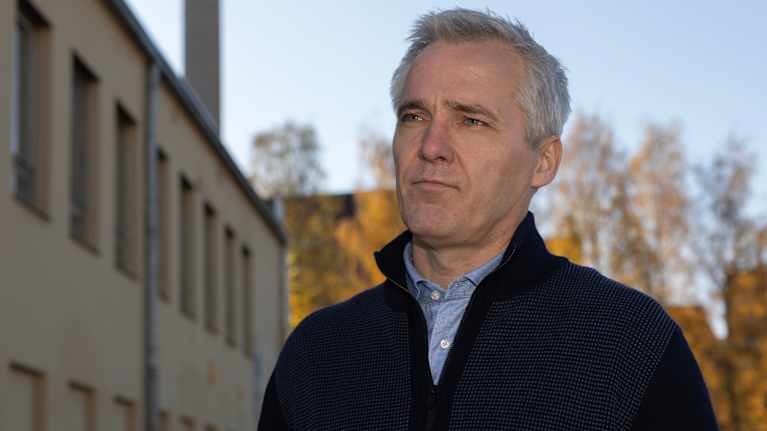 Anders Adlercreutz seisoo ulkona syksyisessä ympäristössä, taustalla näkyy rakennus ja puiden ruskan sävyjä.