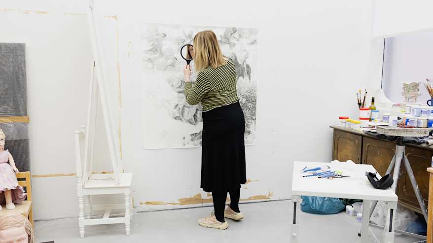 Kuvassa henkilö työskentelee taideteoksen parissa ateljeessa. Hän käyttää peiliä piirtäessä omakuvaa.