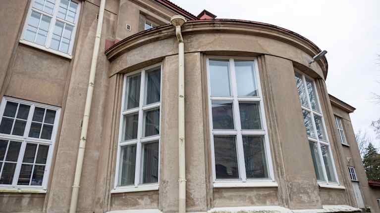 Kaksi kerroksinen harmaa rapattu rakennus, josta tulee pyöreä ulkoneva kaarre alakerran kohdalla.