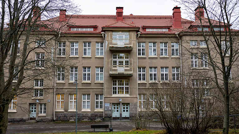 3 kerroksinen harmaa rapattu kerrostalo, jossa punatiilinen katto.