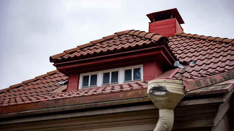 Rakennuksen punatiilinen katto ja siitä pilkottava pieni ikkuna.