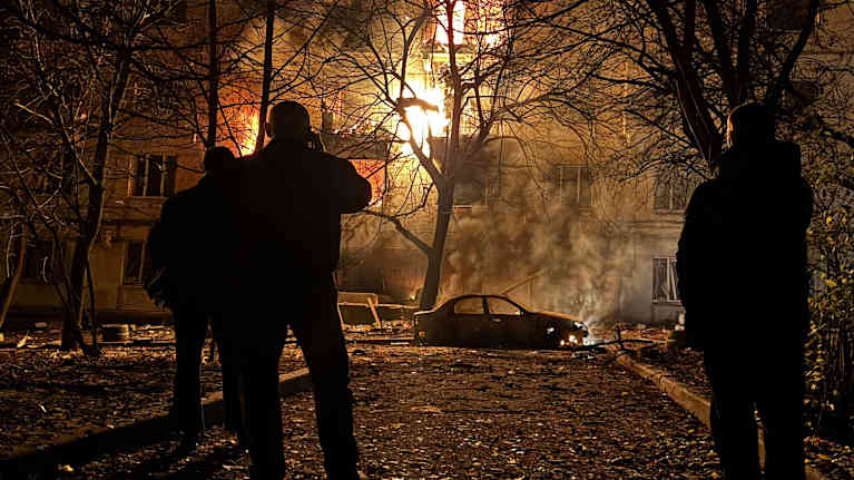 Paikalliset asukkaat katsovat sivusta, kun asuinrakennus syttyy palamaan ilmahyökkäyksen jälkeen Zaporižžjassa.