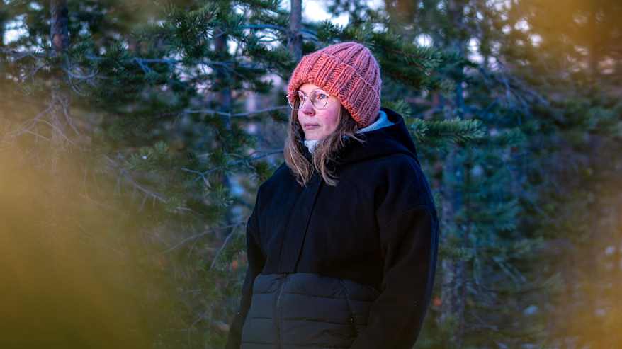 Mari Laaksonen seisoo metsässä talvivaatteisiin pukeutuneena, ympärillään luminen maisema ja vihreitä puita.