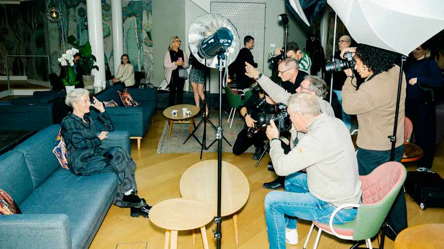 Kuvaustilanne jossa useat valokuvaajat keskittyvät ottamaan kuvia istuvasta henkilöstä.