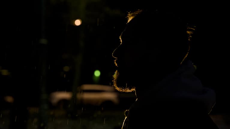 Miehen sivuprofiili hämärässä valaistuksessa, taustalla näkyy vahva valo.