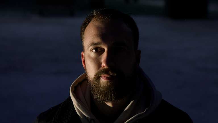 Talvisessa maisemassa henkilö seisoo pimeässä, päällään tumma takki ja vaalea huppari.