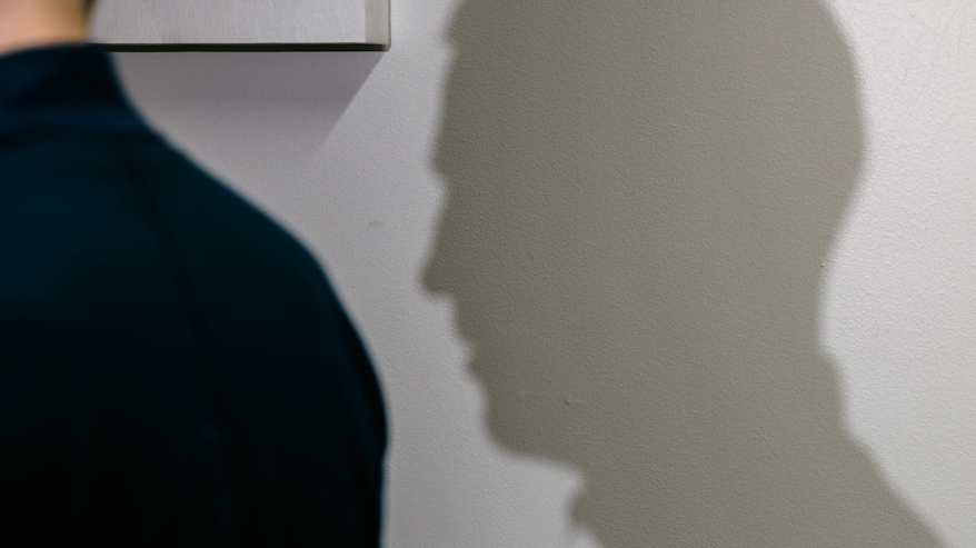 Kuva, jossa varjo paljastaa yksityiskohtia: tuolin edessä istuvan henkilön profiili piirtyy selkeästi seinään.