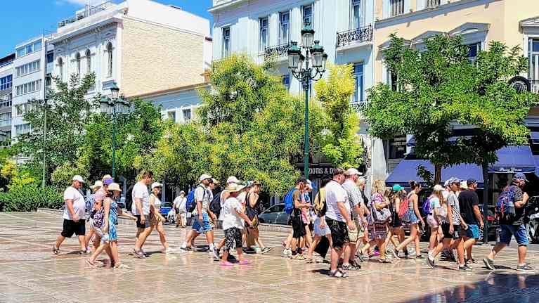 Turistien joukko kävelee kuumuudessa aukiolla. 