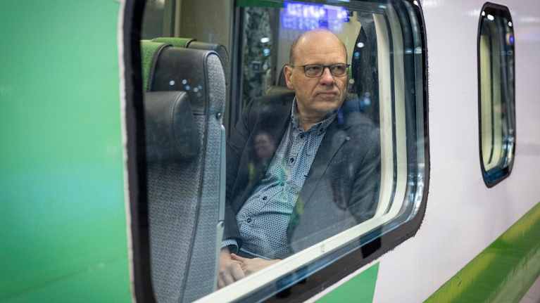 Junan ulkopuolelta otettu kuva, ikkunan takana istuu mies sisällä junassa.