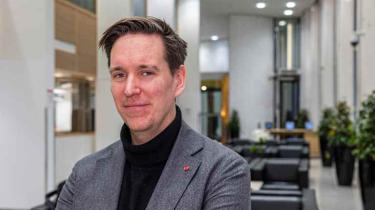 Mies tyylikkäässä harmaassa puvussa seisoo modernin toimistorakennuksen aulassa.